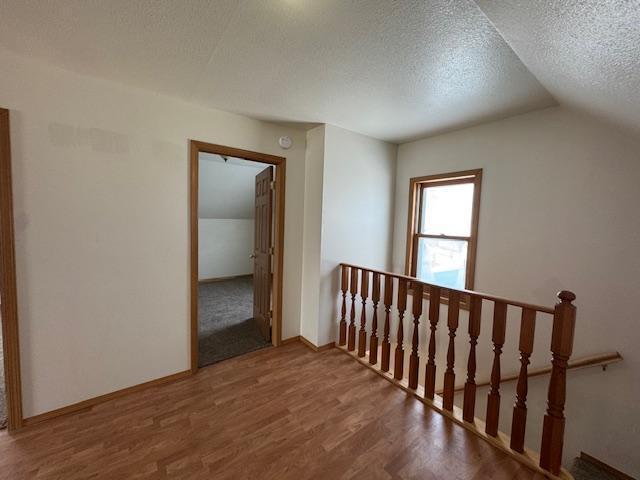 corridor featuring baseboards, wood finished floors, vaulted ceiling, a textured ceiling, and an upstairs landing