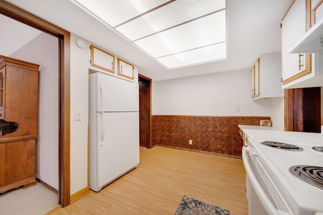 kitchen featuring range hood, light hardwood / wood-style floors, white appliances, wooden walls, and white cabinets