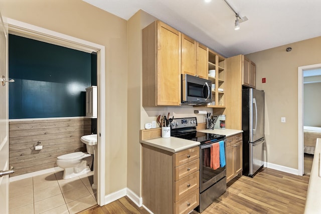 kitchen with wooden walls, light brown cabinetry, stainless steel appliances, and light hardwood / wood-style flooring