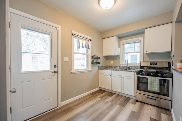 kitchen featuring gas range, sink, light stone counters, and white cabinetry