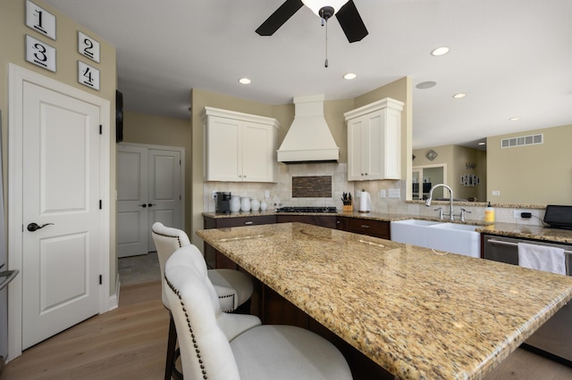 kitchen featuring custom exhaust hood, a breakfast bar, a kitchen island, a sink, and gas cooktop