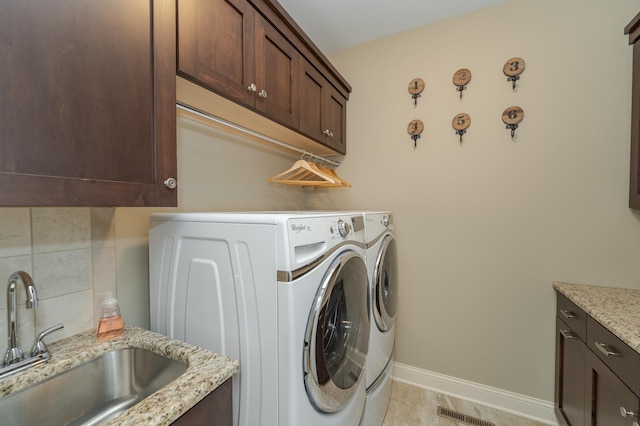 washroom with a sink, cabinet space, washer and clothes dryer, visible vents, and baseboards