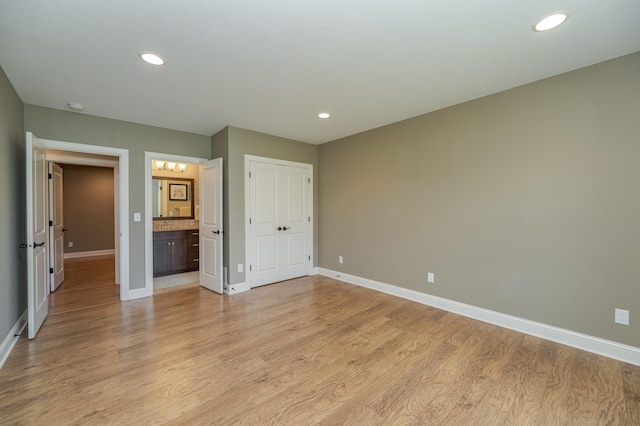 unfurnished bedroom featuring recessed lighting, a closet, ensuite bathroom, baseboards, and light wood-type flooring