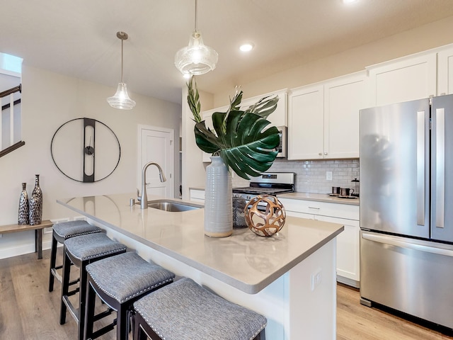 kitchen featuring appliances with stainless steel finishes, a kitchen island with sink, hanging light fixtures, and white cabinets