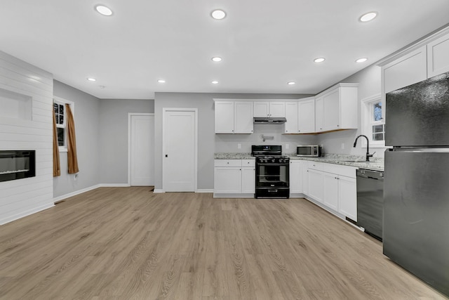 kitchen featuring light stone countertops, light wood-type flooring, a large fireplace, black appliances, and white cabinets