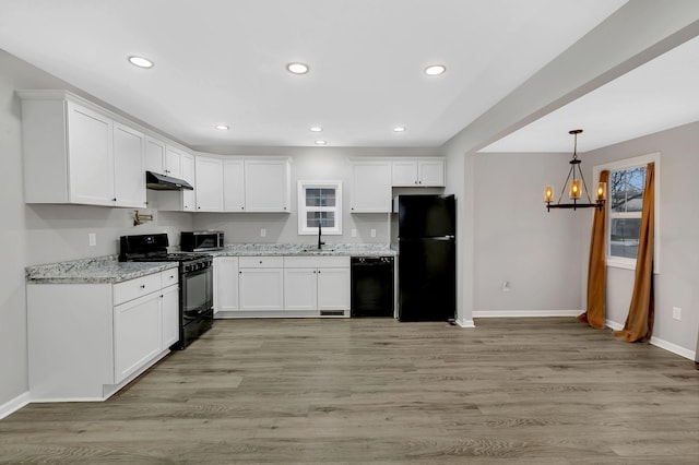 kitchen with sink, light stone counters, pendant lighting, white cabinets, and black appliances