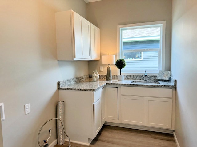 kitchen featuring white cabinetry, sink, light stone counters, and light wood-type flooring