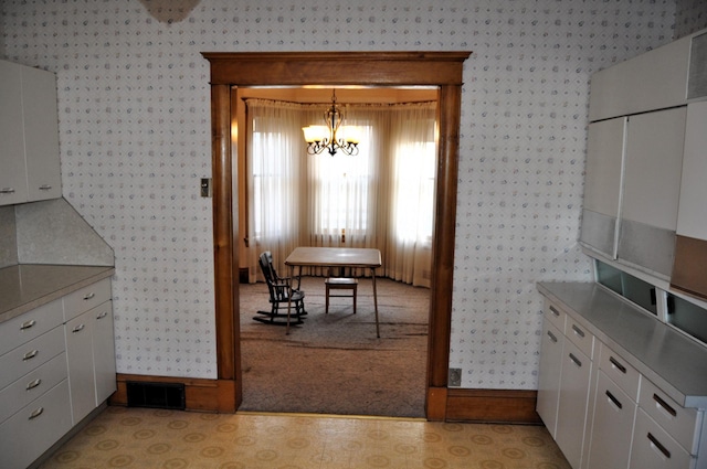 410 5th St, Montevideo, MN 56265 - kitchen featuring wallpapered walls, a chandelier, white cabinetry, and light colored carpet