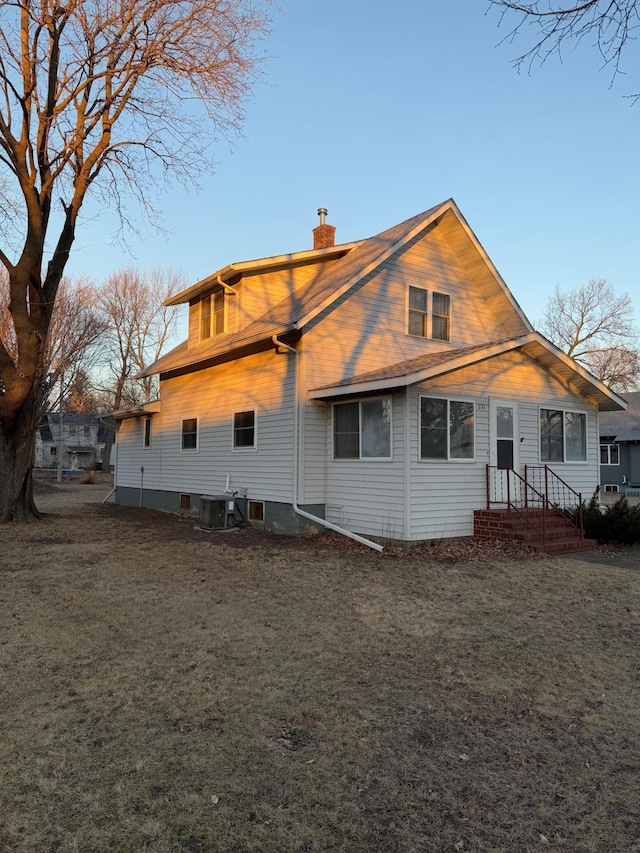 rear view of property featuring central AC unit and a lawn