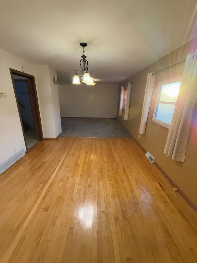 empty room with light wood-type flooring and a chandelier