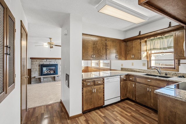 kitchen featuring sink, dishwasher, ceiling fan, dark hardwood / wood-style floors, and a stone fireplace