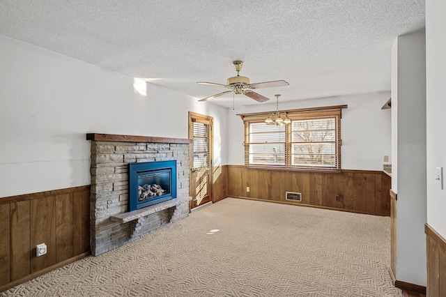 living room with ceiling fan, carpet floors, a textured ceiling, a stone fireplace, and wood walls