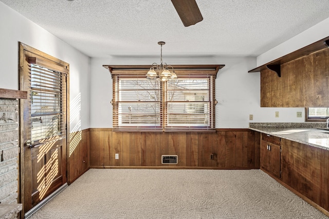 unfurnished dining area with wooden walls, light carpet, and a textured ceiling