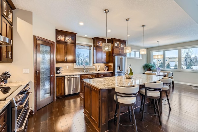 kitchen with dark hardwood / wood-style floors, sink, premium appliances, hanging light fixtures, and a center island