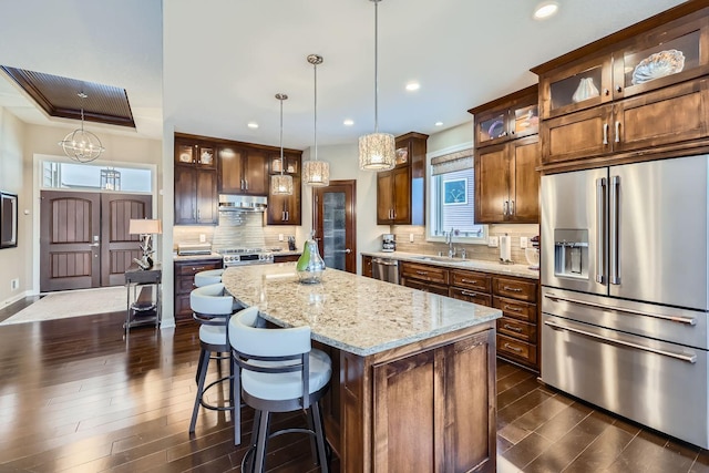 kitchen featuring sink, a center island, pendant lighting, stainless steel appliances, and light stone countertops