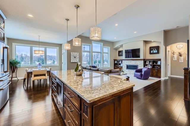 kitchen with a fireplace, decorative light fixtures, a center island, light stone counters, and dark wood-type flooring