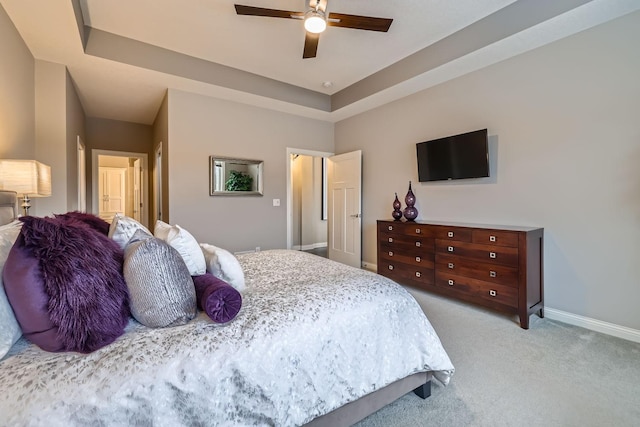 bedroom featuring ceiling fan, a tray ceiling, and light carpet