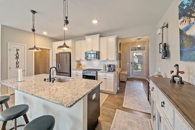 kitchen with a kitchen breakfast bar, sink, decorative backsplash, appliances with stainless steel finishes, and decorative light fixtures