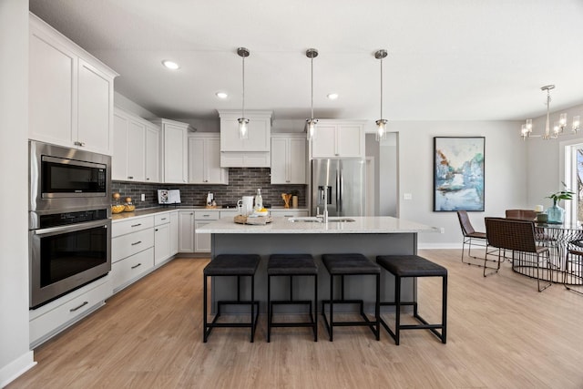 kitchen with appliances with stainless steel finishes, white cabinetry, decorative light fixtures, and a kitchen island with sink