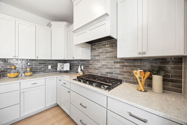 kitchen featuring white cabinetry, light stone counters, tasteful backsplash, stainless steel gas stovetop, and premium range hood