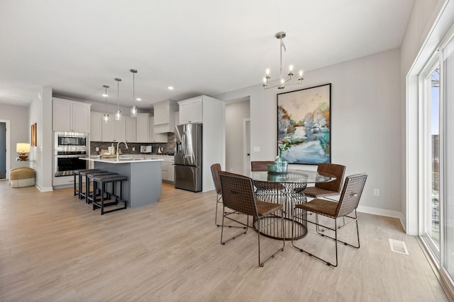 dining space featuring sink, a notable chandelier, and light hardwood / wood-style flooring