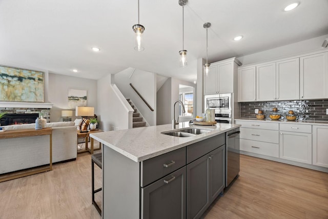 kitchen with sink, stainless steel appliances, decorative light fixtures, white cabinetry, and light hardwood / wood-style floors