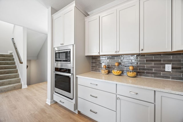 kitchen with light stone countertops, white cabinets, light hardwood / wood-style flooring, and appliances with stainless steel finishes