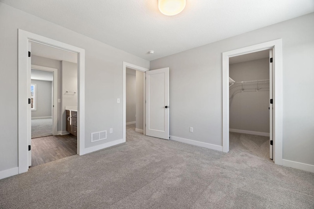 unfurnished bedroom with ensuite bathroom, a closet, light carpet, and a spacious closet