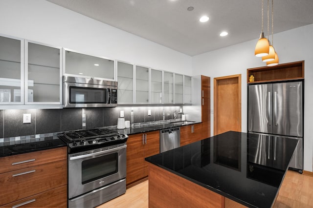 kitchen with sink, stainless steel appliances, light hardwood / wood-style flooring, dark stone counters, and decorative backsplash