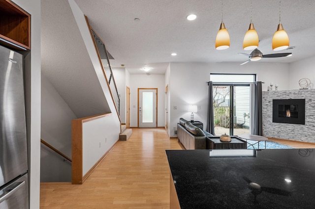 kitchen featuring ceiling fan, light hardwood / wood-style flooring, hanging light fixtures, and a tiled fireplace