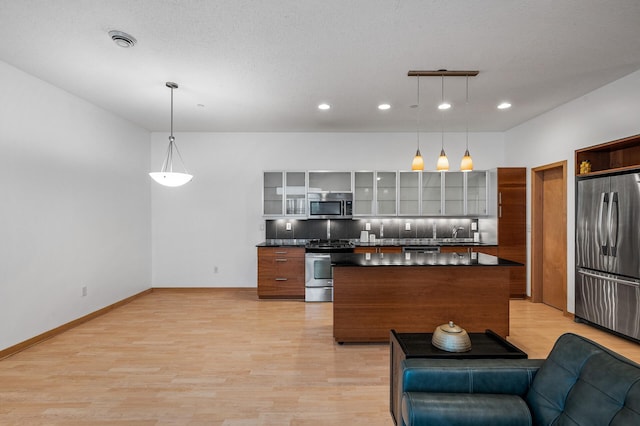 kitchen featuring pendant lighting, light hardwood / wood-style flooring, decorative backsplash, appliances with stainless steel finishes, and a kitchen island