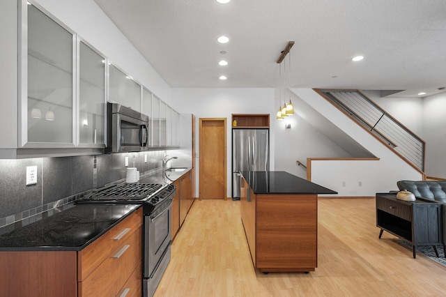 kitchen featuring a center island, hanging light fixtures, light hardwood / wood-style flooring, decorative backsplash, and appliances with stainless steel finishes