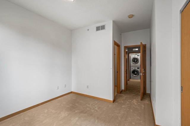 carpeted empty room with stacked washer and dryer