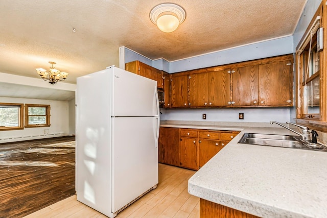 kitchen with sink, a baseboard radiator, a notable chandelier, white fridge, and light hardwood / wood-style floors