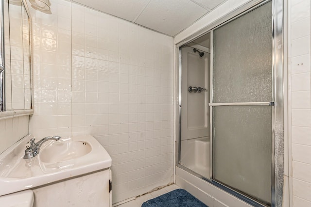 bathroom featuring vanity, a shower with door, tile walls, and a paneled ceiling