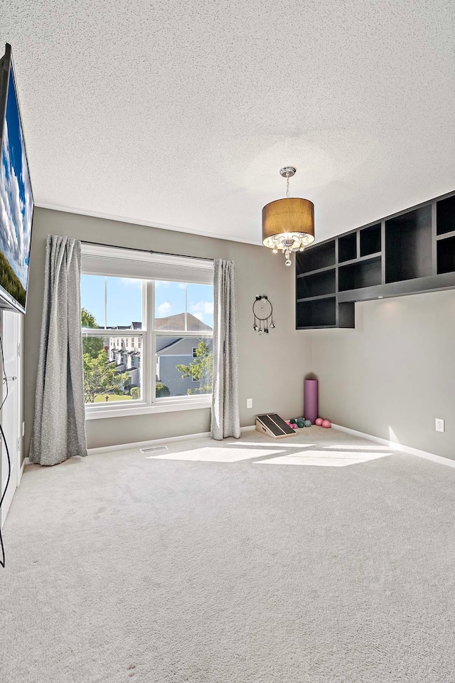 unfurnished room with carpet, a textured ceiling, and an inviting chandelier