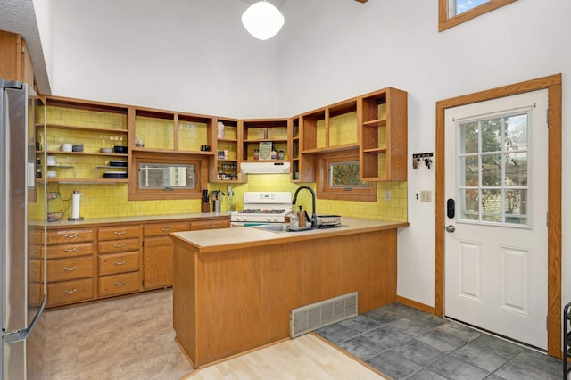 kitchen with stainless steel refrigerator, white gas range, sink, kitchen peninsula, and a towering ceiling