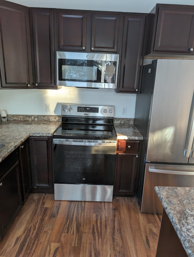 kitchen with stainless steel appliances, dark hardwood / wood-style flooring, stone countertops, and dark brown cabinets