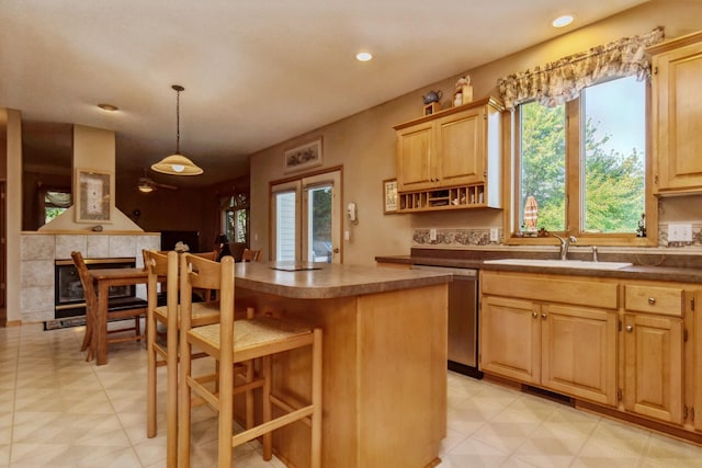 kitchen with a tiled fireplace, light brown cabinets, stainless steel dishwasher, and a sink