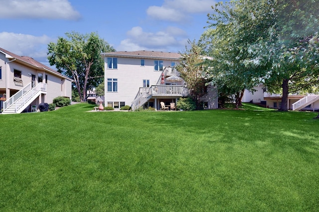 rear view of house with a yard, a wooden deck, and stairs