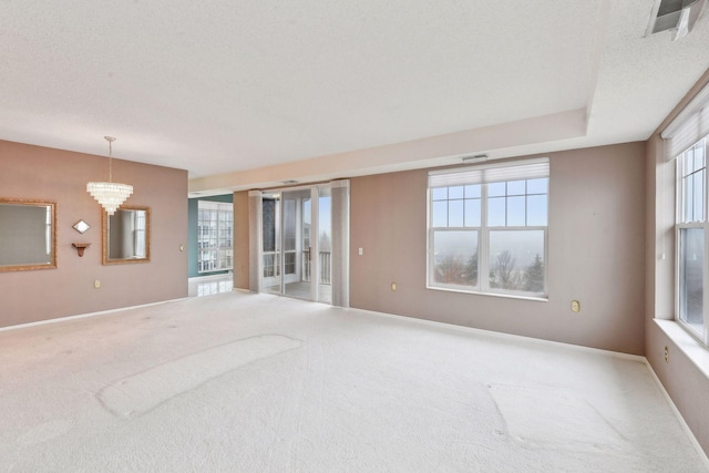 carpeted empty room featuring a textured ceiling and a notable chandelier