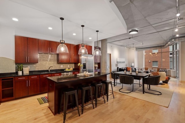 kitchen featuring sink, light hardwood / wood-style flooring, decorative light fixtures, stainless steel fridge with ice dispenser, and a breakfast bar area