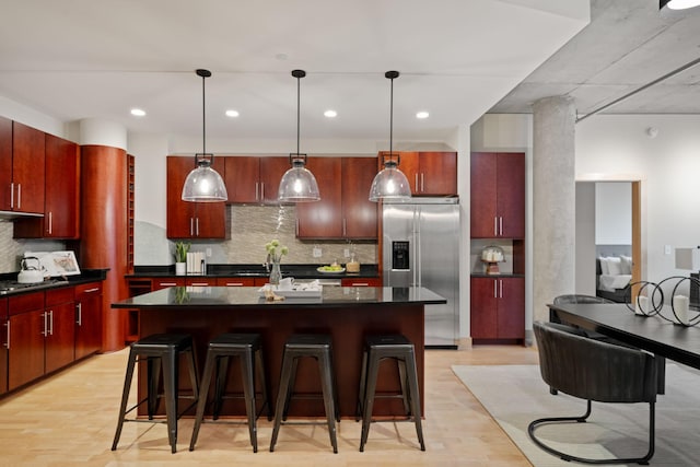 kitchen featuring stainless steel fridge, a kitchen island, hanging light fixtures, and a kitchen breakfast bar