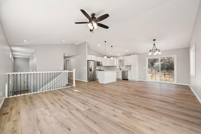 unfurnished living room with light wood-type flooring, ceiling fan with notable chandelier, vaulted ceiling, and sink