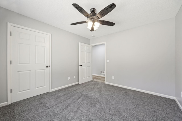 unfurnished bedroom with a textured ceiling, a closet, dark carpet, and ceiling fan