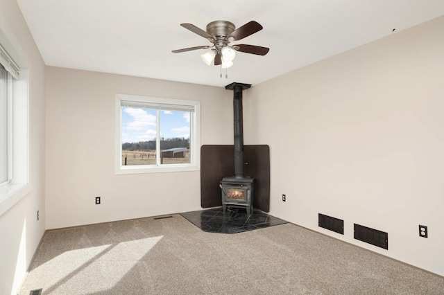 unfurnished living room with carpet flooring, visible vents, ceiling fan, and a wood stove