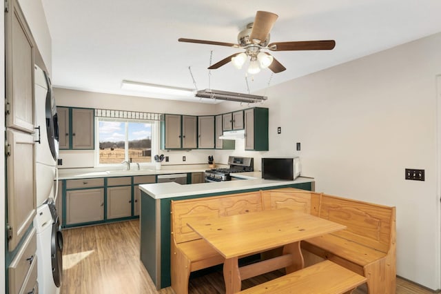 kitchen featuring a peninsula, ceiling fan, light wood-style floors, appliances with stainless steel finishes, and stacked washer / dryer