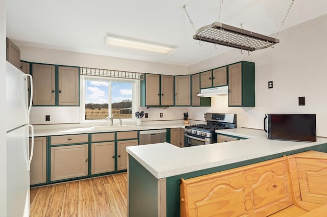 kitchen featuring under cabinet range hood, light countertops, appliances with stainless steel finishes, a peninsula, and a sink