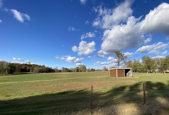 view of yard featuring an outbuilding, a rural view, and fence