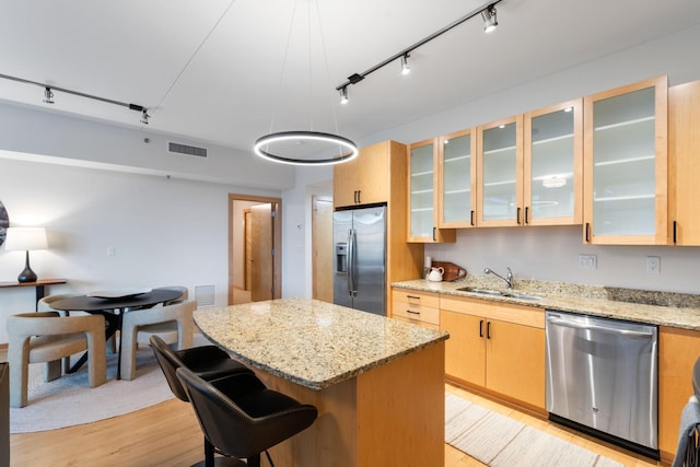 kitchen with light stone countertops, sink, stainless steel appliances, light brown cabinetry, and a kitchen island